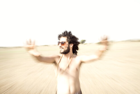 Bare chested man with sunglasses reaching out in desert - BMAF000148