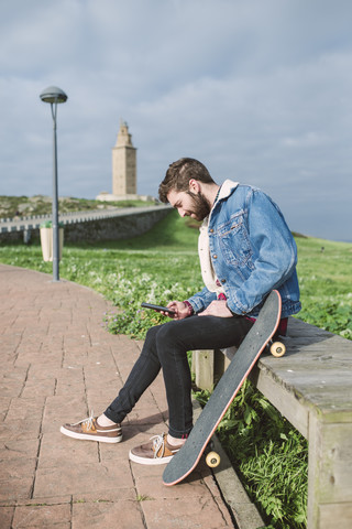 Spanien, A Coruna, junger Mann mit Longboard und Smartphone, lizenzfreies Stockfoto