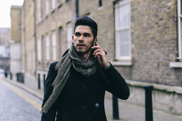 Young casual businessman walking in the street using mobile phone - BOYF000216