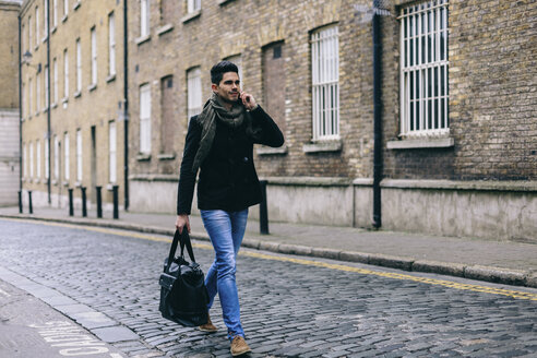 Young casual businessman walking in the street using mobile phone - BOYF000217