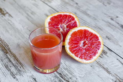 Aufgeschnittene Grapefruit und Glas Grapefruitsaft auf Holz, lizenzfreies Stockfoto