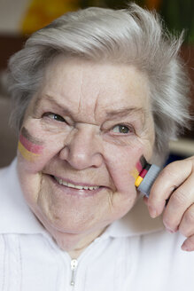 Porträt einer selbstbewussten älteren Frau, die sich die deutschen Nationalfarben auf die Wange malt - MIDF000720