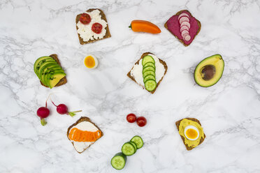 Wholemeal bread slices with different spreads and toppings on white marble - LVF004668