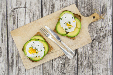 Vollkornbrotscheiben mit geschnittener Avocado und pochierten Eiern auf Holzbrett - LVF004672