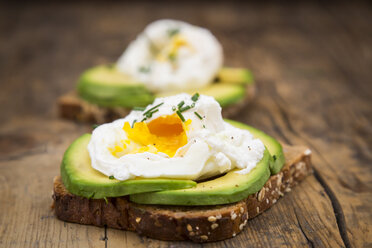 Vollkornbrotscheiben mit Avocadoscheiben und pochierten Eiern auf Holz - LVF004673