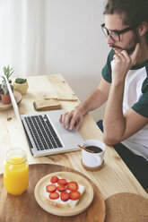 Young man using laptop while having breakfast - RTBF000015