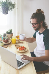 Junger Mann mit Laptop beim Frühstück - RTBF000016