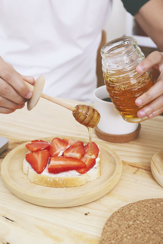 Junger Mann mit Honig auf Toast mit Erdbeeren, lizenzfreies Stockfoto