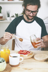 Young man putting honey on toast with strawberries - RTBF000021