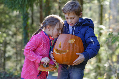 Junge und Mädchen begutachten Halloween-Kürbis im Wald, lizenzfreies Stockfoto