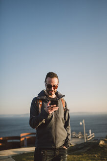 Mann mit Sonnenbrille schaut auf sein Smartphone - RAEF000953