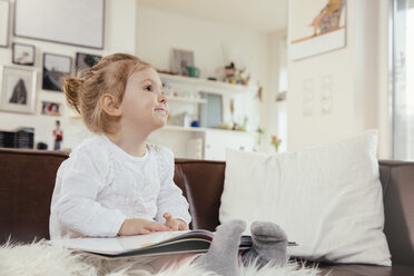 Glückliches kleines Mädchen sitzt mit einem Buch auf der Couch - MFF002884