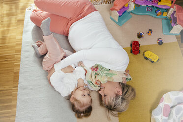 Schwangere Mutter und kleine Tochter kuscheln auf Teppich zu Hause - MFF002902