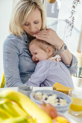 Little girl crying in mother's arms at breakfast table - MFF002910