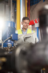 Mann mit reflektierender Weste betrachtet ein Gerät in einer Industrieanlage - FKF001726