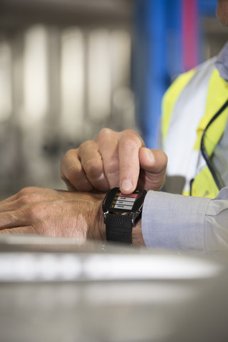 Mann benutzt Smartwatch in Industrieanlage, lizenzfreies Stockfoto