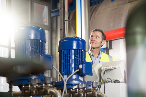 Mann mit Warnweste sieht sich in einer Industrieanlage um, lizenzfreies Stockfoto