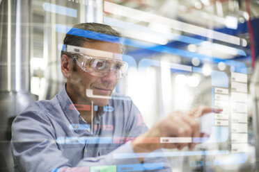 Man wearing safety goggles using transparent touchscreen device - FKF001759