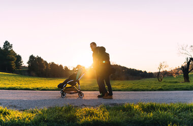 Ehepaar auf einem Spaziergang mit ihrem Baby im Kinderwagen bei Sonnenuntergang - GEMF000798