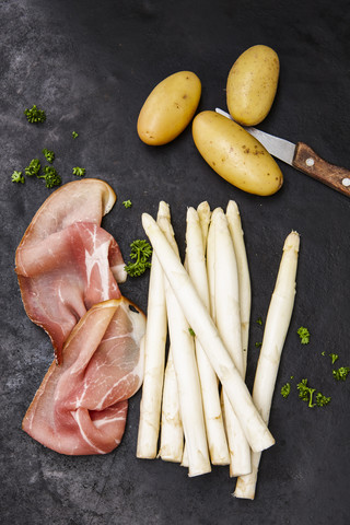 Rohe Kartoffeln und Scheiben von rohem Schinken, weißer Spargel und Petersilie, lizenzfreies Stockfoto