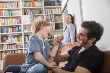 Father and son playing on sofa, mother watching in background - FMKF002517