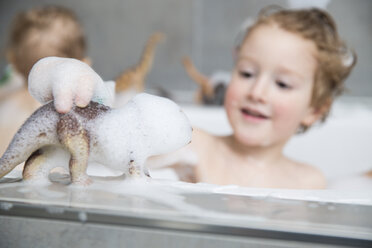 Kleiner Junge sitzt mit seinem Bruder im Schaumbad und spielt mit Dinosaurier-Figuren - FMKF002524