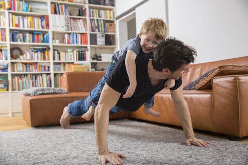 Vater macht Liegestütze im Wohnzimmer mit Sohn auf seinem Rücken - FMKF002527