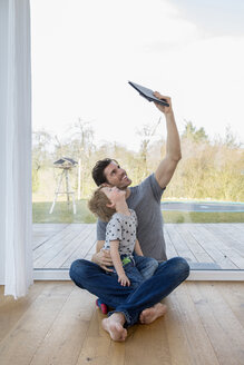Vater und Sohn sitzen auf dem Boden und benutzen ein digitales Tablet - FMKF002531