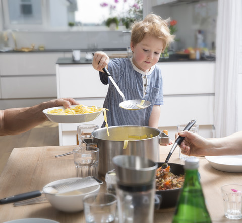 Stolzer kleiner Junge serviert Nudeln in der Küche, lizenzfreies Stockfoto