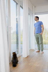 Man at home standing at window looking out - FMKF002557