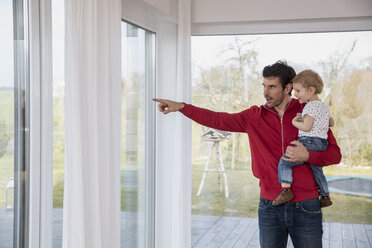 Father holding son in his arms, pointing out of window - FMKF002560