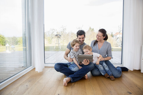 Glückliche Familie sitzt auf dem Boden und benutzt ein digitales Tablet - FMKF002561