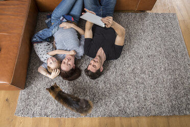 Happy family lying on floor, using digital tablet - FMKF002580