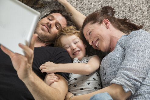 Happy family lying on floor, using digital tablet - FMKF002581