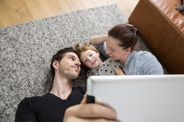 Glückliche Familie auf dem Boden liegend, mit digitalem Tablet - FMKF002582