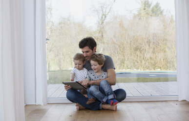 Father and sons sitting on floor using digital tablet - FMKF002585