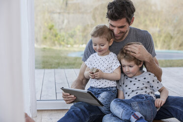 Vater und Söhne sitzen auf dem Boden und benutzen ein digitales Tablet - FMKF002586