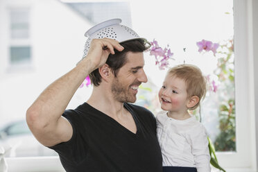 Father and son playing at home, using colander as hat - FMKF002593