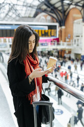 UK, London, Junge Frau benutzt Mobiltelefon am Bahnhof - MGO001569