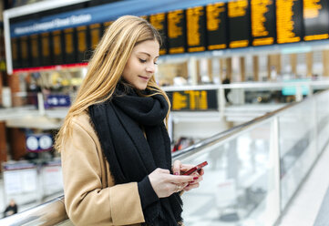 UK, London, Junge Frau benutzt Mobiltelefon am Bahnhof - MGO001572