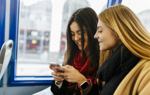 UK, London, Zwei junge Frauen benutzen ein Smartphone im Bus - MGOF001575