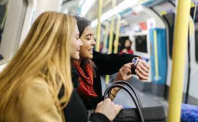 UK, London, Zwei junge Frauen in der U-Bahn schauen auf eine Smartwatch - MGO001589