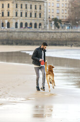 Spanien, Gijon, Mann spielt am Strand mit seinem Hund - MGOF001594