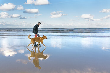 Mann, der mit seinem Hund am Strand spazieren geht - MGOF001600