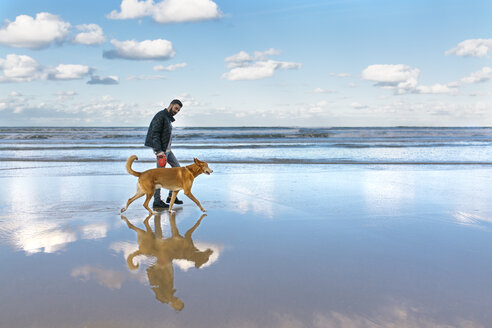 Mann, der mit seinem Hund am Strand spazieren geht - MGOF001600