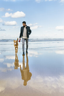 Mann, der mit seinem Hund am Strand spazieren geht - MGOF001601