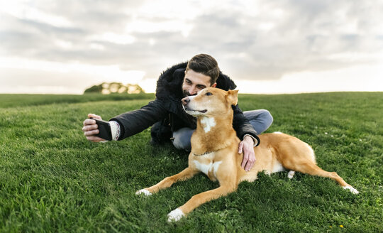 Mann macht ein Selfie mit seinem Hund auf einer Wiese - MGOF001611