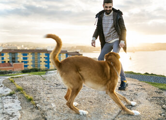 Spain, Gijon, man playing with his dog - MGOF001617