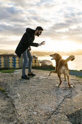 Spain, Gijon, man playing with his dog in the evening - MGOF001618