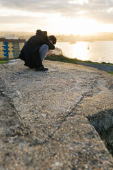 Spanien, Gijon, Mann hockt in der Abenddämmerung auf einer Mauer und bedeckt sein Gesicht mit dem Arm - MGOF001619